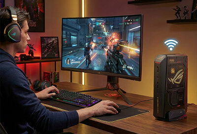 person gaming with wireless symbol above NUC next to monitor