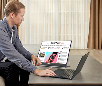 Man browsing laptop with monitor in the distance showing news feed