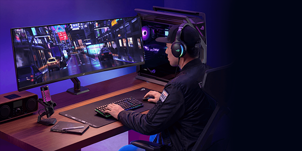 Key visual of desktop setup with ultra-wide curved monitor attached to ROG Ergo arm, with gamer sat behind the desk.