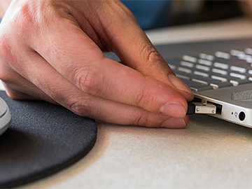 USB-BE92 Nano adapter being inserted into a laptop by hand.