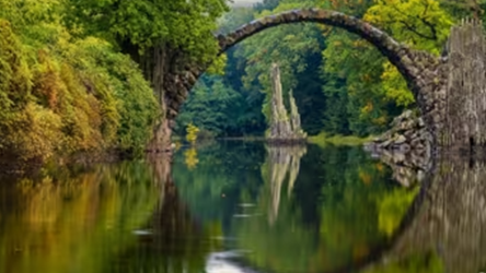 Old bridge reflecting into a still river with forrested land around.
