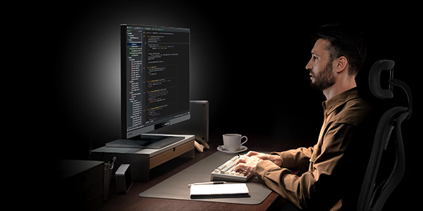Man sat at desk working on BenQ Programming monitor in a dark environment.