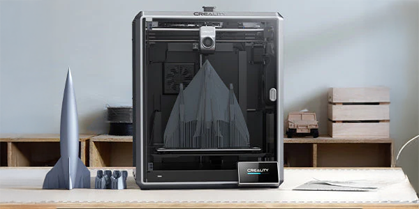 Front view of K1 Max 3D printer atop a desk next to a 3D printed rocket.