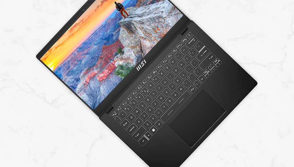 MSI Modern 14 laptop open flat, tilted on a 45 degree angle, with scenic cliff face view on-screen.