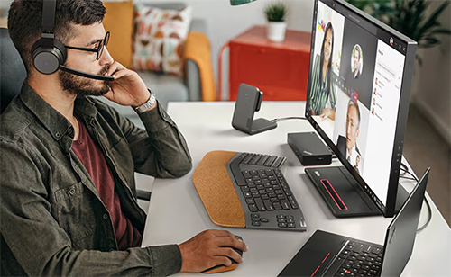 Photo of a man in a dark green shirt and glasses using the ThinkPad Dock with a monitor and also connected to a laptop