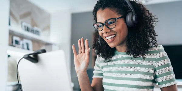 Woman waving at C720 webcam mounted atop her monitor in home/office.