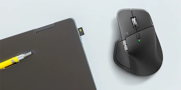 Top down angle of MX Master 4 mouse next to closed laptop with wireless USB-C receiver attached.