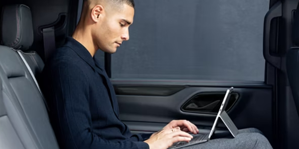 Man sat in car with Surface Pro on knee typing on his attached keyboard
