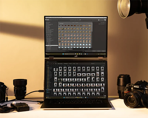 Front view of the monitor connected to a laptop with photographs on the screen and photography equipment on the desk around it
