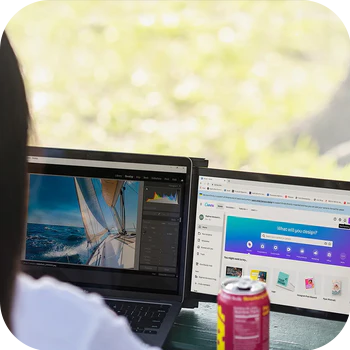 person with long hair viewing monitor in front of window with can of soda