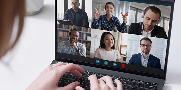 Laptop on desk with video conference on-screen while fingers type on the keyboard.