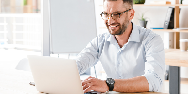 Man with smile working on laptop at a desk in a bright modern office.
