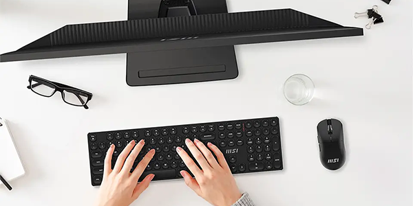 Top down of FORGE keyboard combo with monitor setup on desk with fingers typing.