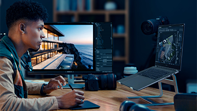 Man set at desk using graphics tablet while looking at laptop.