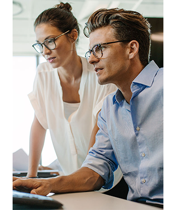 Lifestyle image of a female and male doctor wearing glasses looking at a computer
