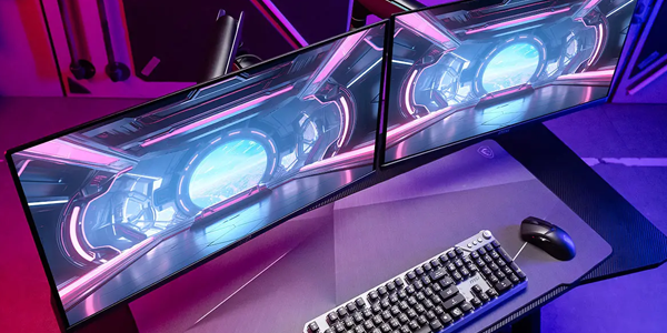 Monitor mounted to arm attached to gaming desk with keyboard and mouse atop.
