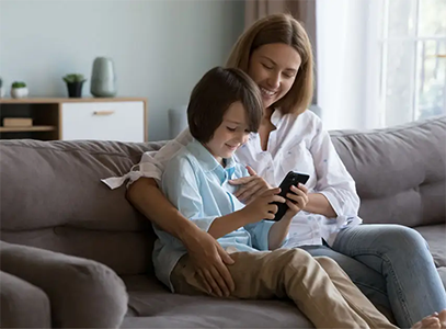 Mother and child sat on sofa using mobile device.