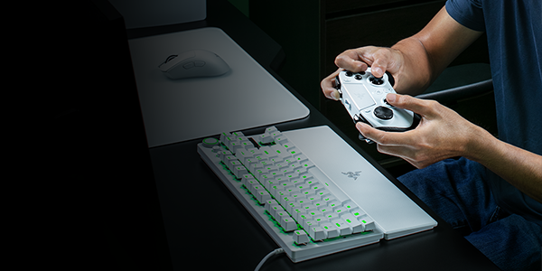 Gamer at desk playing on Raiju V3 Pro controller with Razer keyboard/mouse/mousemat on the desk.