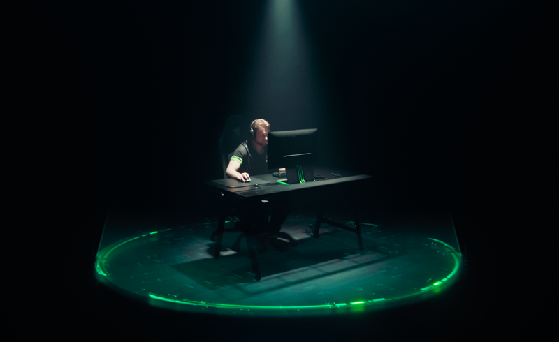 Esports professional sat at desk under spotlight with graphic overlay of a defined area illustrating noise-cancelling capabilities 