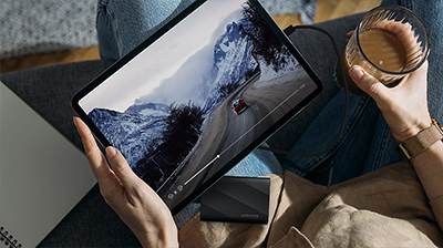 Person holding tablet with SSD in lap and coffee in other hand