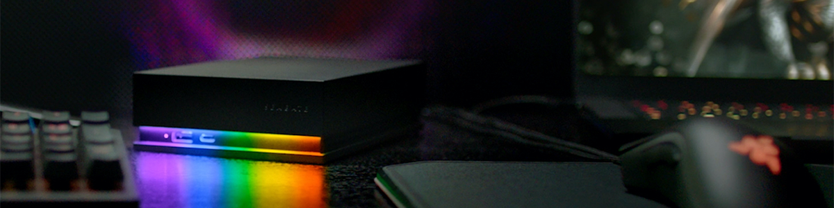 Key visual FireCuda gaming hard drive, illuminated on a glossy desk beside PC peripherals.
