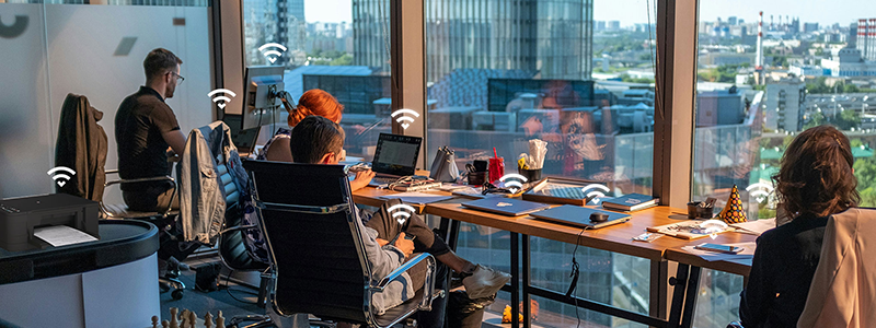 Workers in sky-rise office using WiFi devices with pulse graphic illustrated over their devices.