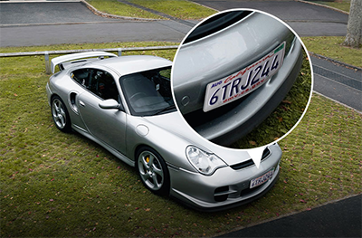 Silver sports car parked on grass with details of number plate enlarged.