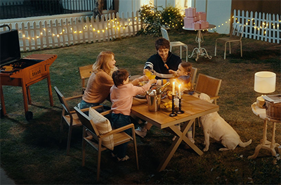 Family sat round a table in garden at night.