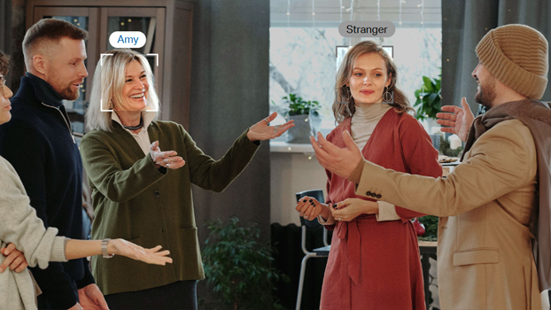 Face recognition placing border and nametag around the head of a woman named Amy and a stranger as they stand amongst people. 