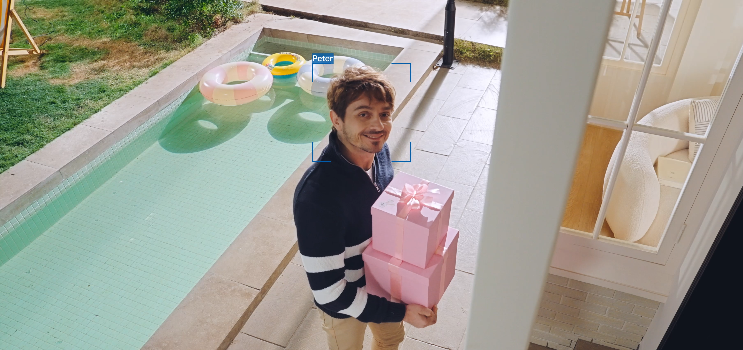 Man holding gift outside house, face detected by blue outline.