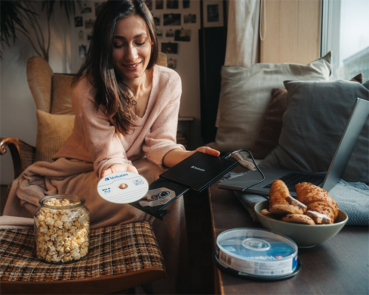 Woman on sofa holding the external blu-ray writer in one hand and a blu-ray disc in the other to highlight its portable convenience