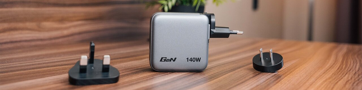 Mini GaN charger on a wooden desk with EU plug attachment connected. UK and US plug attachments on the desk, either side of the charger.