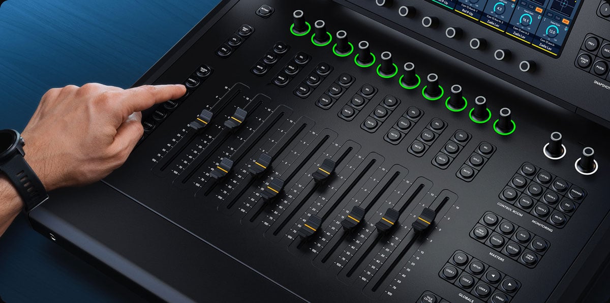 Close-up of a person's hand adjusting a fader on a professional digital audio mixing console with illuminated controls