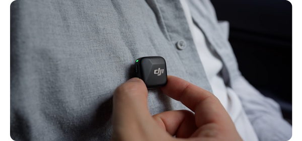 Person activating DJI Mic Minis Noise Cancellation button while wearing light grey button shirt