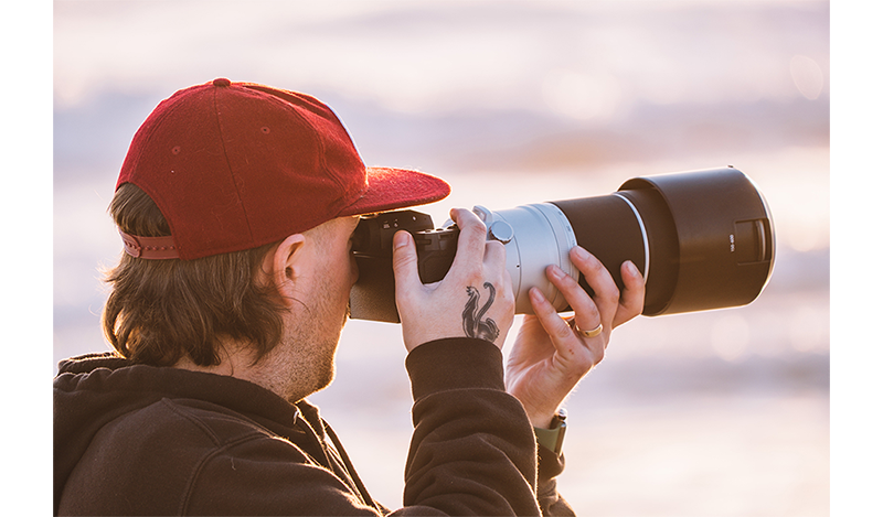 Photograppher wearing black hoodie and red baseball cap using Fujifilm XF150-600mm Lens on fuji xt5 camera