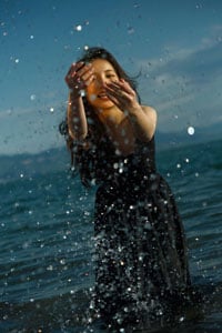 Fujifilm XF16-55mm F2.8 R LM WR II sample image of female model splashing in ocean wearing black dress against blue sky