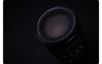 photograph of Fujifilm XF16-55mm F2.8 R LM WR II covered with water dropplets on black background