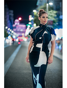 Woman wearing a blue and white all in one dress standing on a street with neon lights in the distance