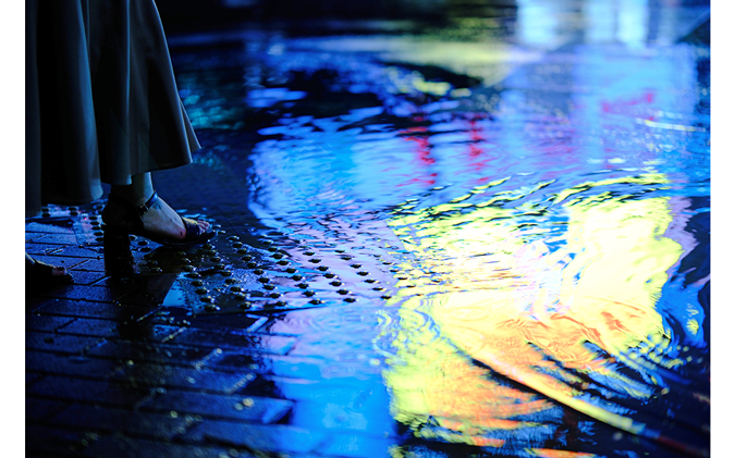 Womans foot walking through a puddle illuminated by street signs at a road crossing