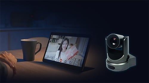 PTZ conference camera next to a tablet displaying a video call on a desk