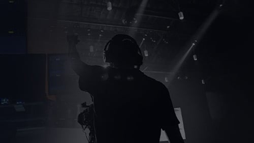 Silhouette of a cameraman wearing headphones operating a professional video camera in a dark studio stage with lights