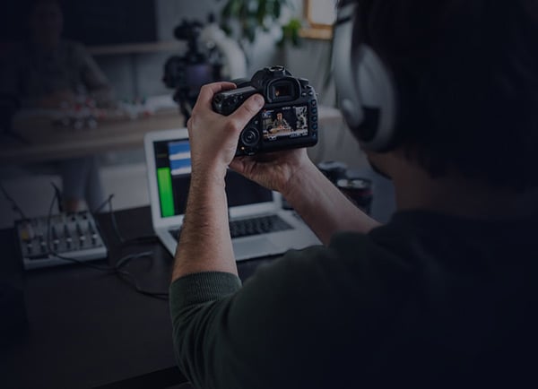 A person holding a camera while editing video content on a laptop in a home studio