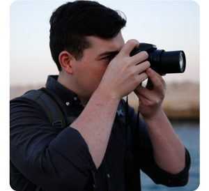 person holding LUMIX DZ82D bridge camera to their eye shooting photographs in front of river