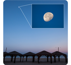 LUMIX FZ82D wide angle sample photograph of sunset above beach huts with clear blue sky and Zoom on moon