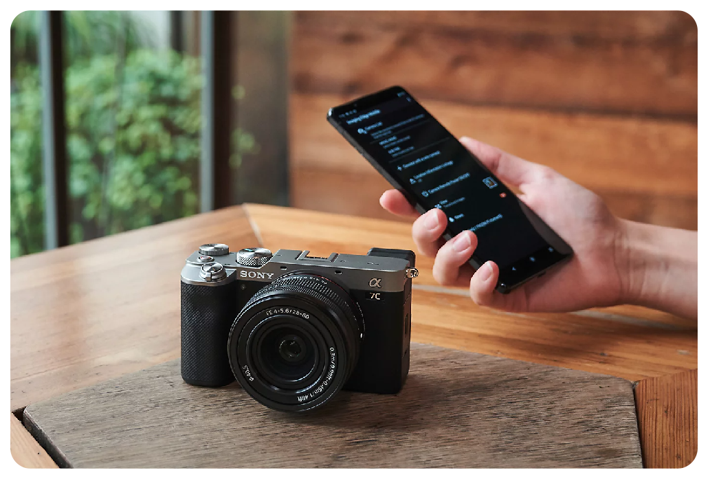 Sony A7C sat on wooden table with person holding their smartphone in hand