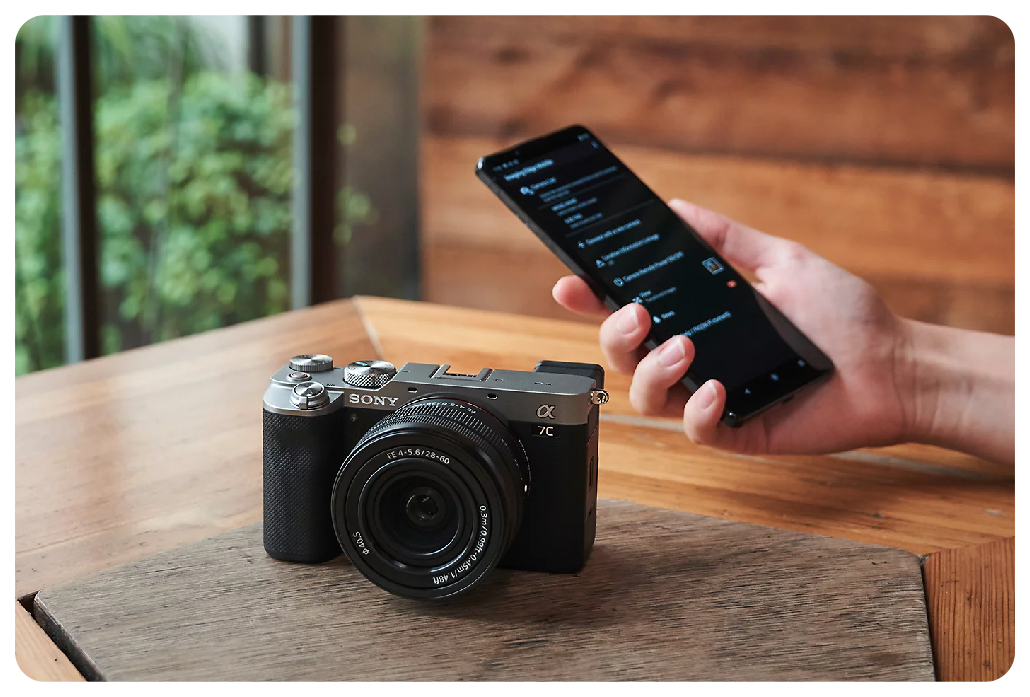 Sony A7C sat on wooden table with person holding their smartphone in hand