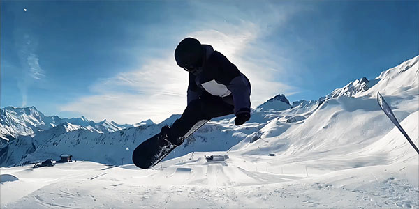Snowboarder mid-air performing a jump trick on a snow-covered mountain slope