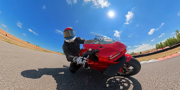 a rider in protective track gear leaning a red sport motorcycle into a sharp turn captured using the dji osmo 360 II