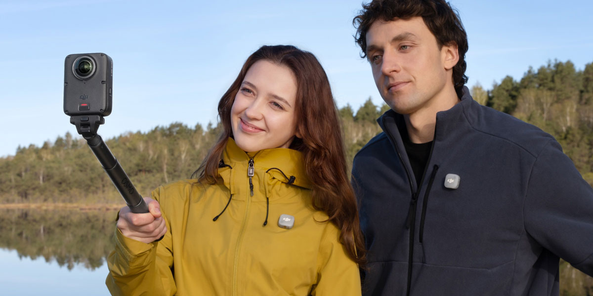 Man and woman using an action camera on an extension pole near a lake