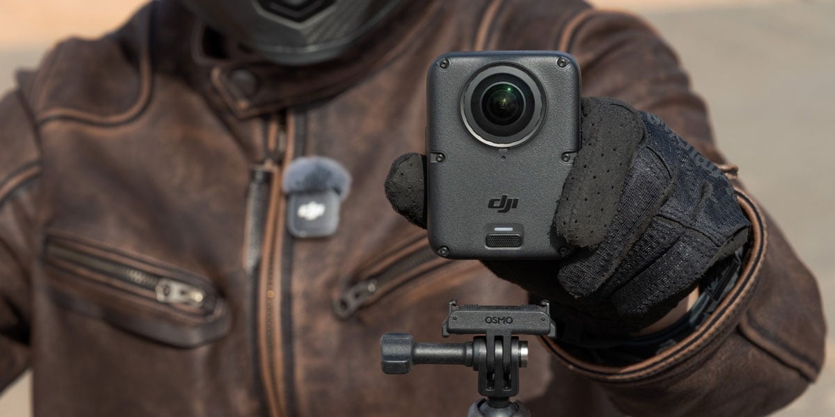 A person wearing a leather motorcycle jacket and gloves holding a DJI Osmo 360 II action camera